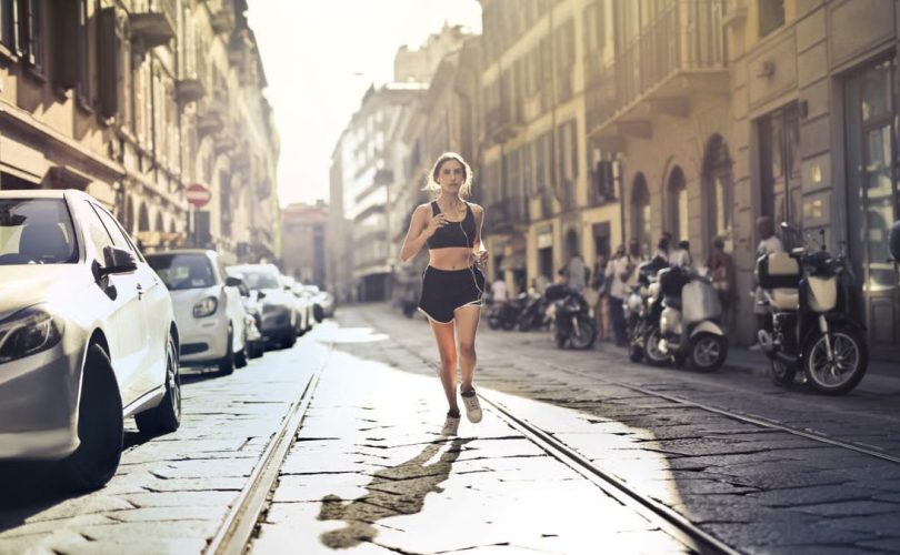 Energetic woman jogger running down a city street in active wear on a sunny day.